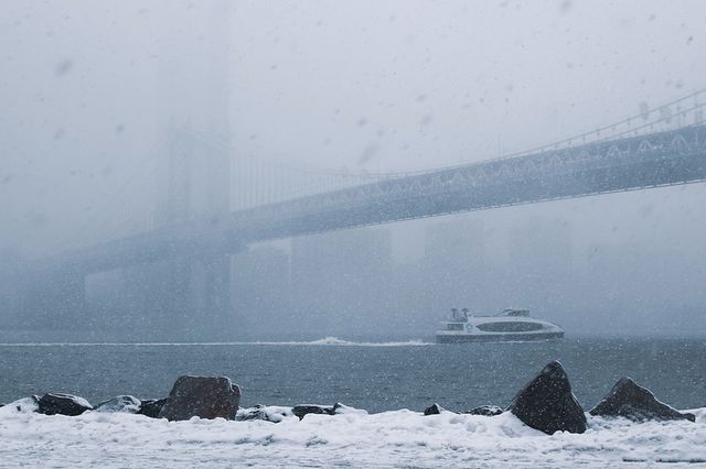 a ferry rides under a snowy Brooklyn Bridge
